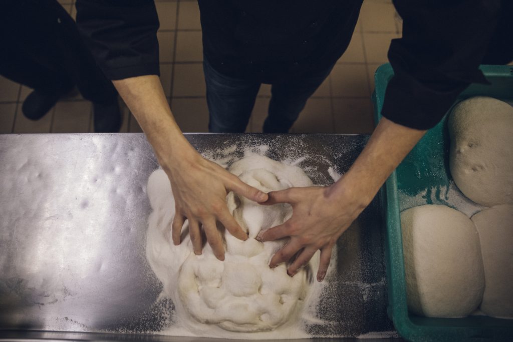 A chef hand-pressing pinsa dough.